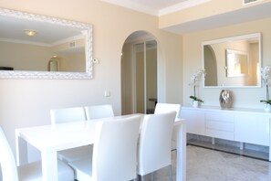A modern dining area with a white table and chairs, a large mirror, and a white cabinet with a plant. - RDR110 - Apt. Dama de Noche 6 (Marbella)