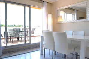 Een moderne eethoek met een witte tafel en stoelen, een grote spiegel en een uitzicht door glazen deuren op een buitenruimte.