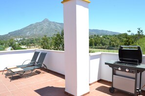 Une terrasse équipée d’un barbecue, de deux chaises longues et offrant une vue sur la montagne.