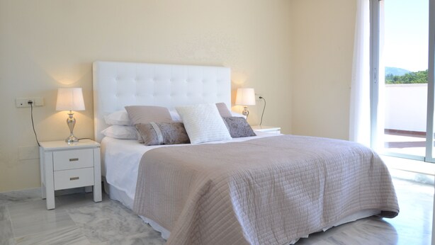 A bedroom with a large bed, two bedside tables, and a view through a window.