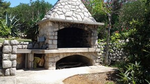 Een buitenoven van natuursteen voor pizza, met schoorsteen, omringd door groen en bomen.