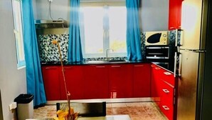 Een keuken met rode kastjes, een raam met blauwe gordijnen en een betegelde spatwand.