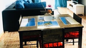 Een moderne woonkamer met een donkergroene bank, een eettafel met rode kussens en een televisie op een witte kast.
