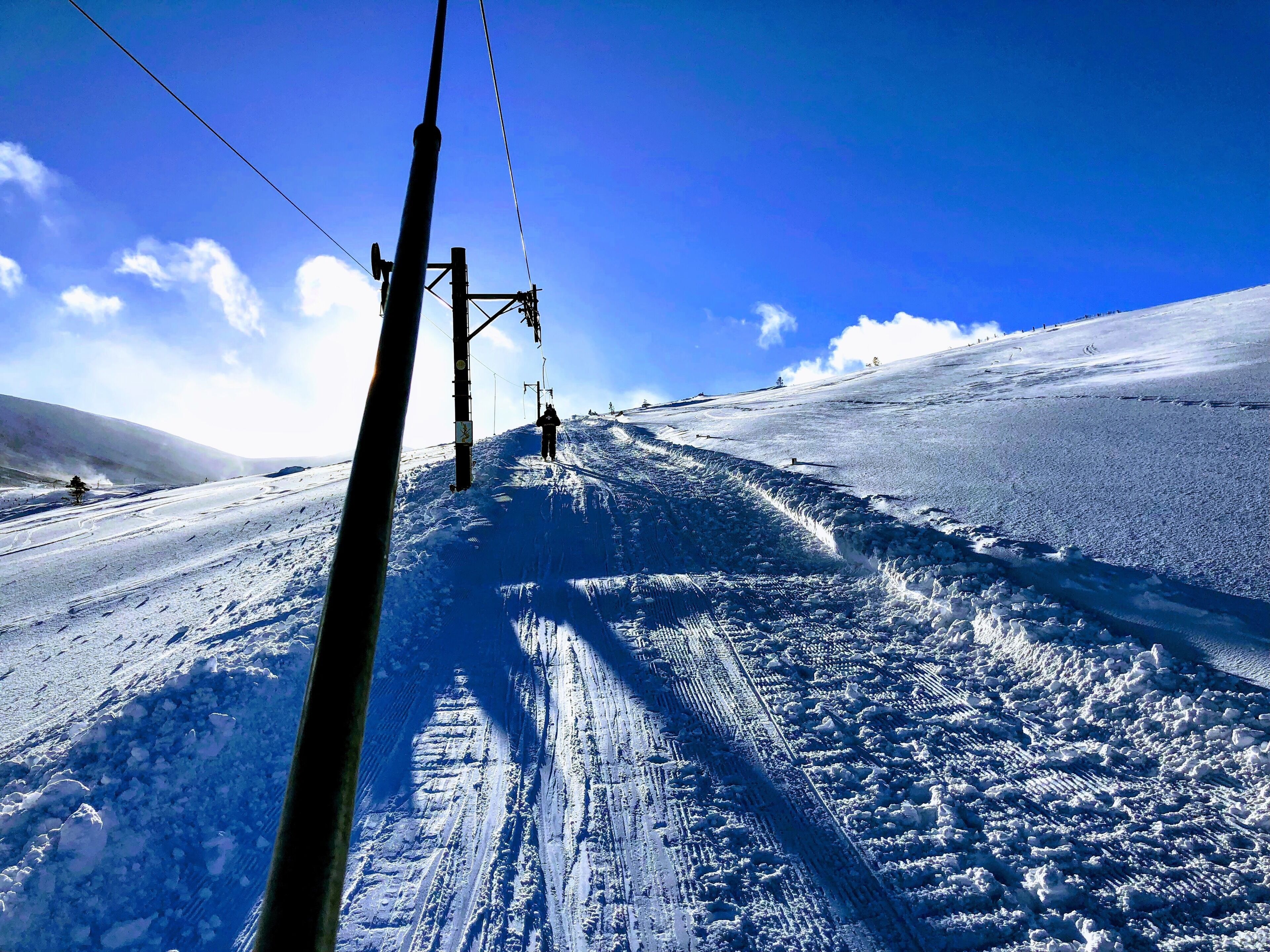 A ski slope with a clear sky, ski lift cables, and tracks.