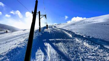A ski slope with a clear sky, ski lift cables, and tracks.