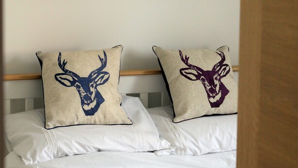 Ein Schlafzimmer mit einem Bett, zwei Kopfkissen mit Hirschmotiven und einem Walddekor über dem Bett.