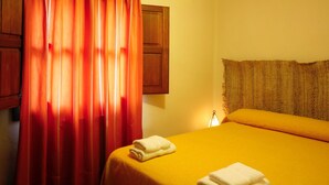 Une chambre avec un lit, une tête de lit en bois, un rideau rouge et une petite table avec une lampe.