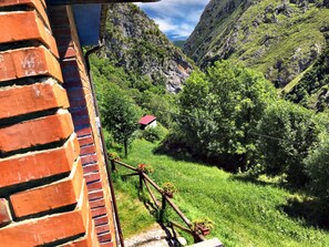A brick wall with a wooden railing overlooking a lush green valley with a small building in the distance.