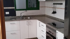 A kitchen with white cabinets, a stainless steel sink, a window with green trim, and a tiled floor. - Apartment in quiet area and close to the beach (Tías)