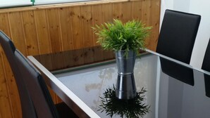 A glass-top table with four black chairs, a potted plant, and a wooden paneled wall in the background. - Apartment in quiet area and close to the beach (Tías)