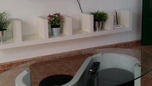 A modern living room with a flat-screen TV mounted on the wall, a glass coffee table, and a white console table with potted plants. - Apartment in quiet area and close to the beach (Tías)