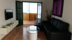 A modern living room with a black leather sofa, a glass coffee table, and a TV mounted on the wall. - Apartment in quiet area and close to the beach (Tías)