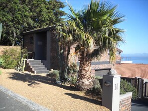 A two-story house with a brick exterior, a palm tree in front, and a view of the ocean.