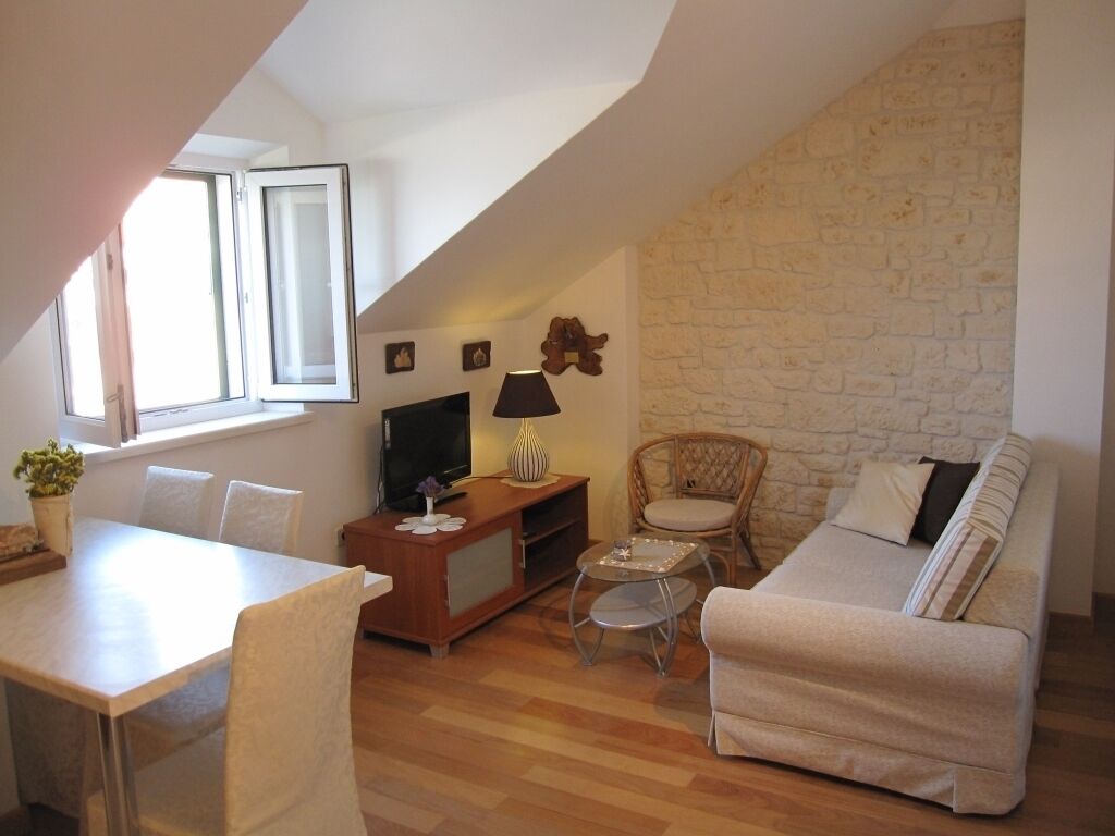 A cozy living room with a stone wall, a sofa, a TV, a lamp, and a dining area with chairs and a table.