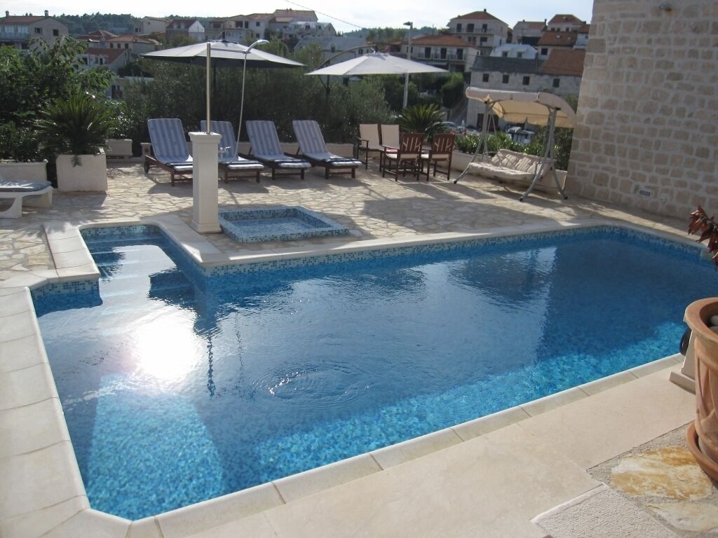 Ein rechteckiger Pool mit einer gefliesten Kante, umgeben von Liegestühlen und Sonnenschirmen.