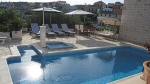 Une piscine rectangulaire dont le bord est recouvert de carrelage, entourée de chaises longues et de parasols.