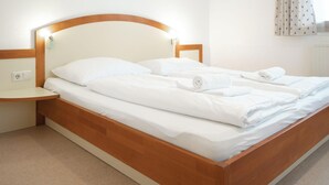 A double bed with white linens and towels, a wooden headboard, a bedside table, and a power outlet. - Seilergasse Apartments - TOP 4, city center (Zell am See)