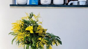 Un cartello di benvenuto con lettere di legno, un vaso con fiori gialli ed elettrodomestici su uno scaffale.