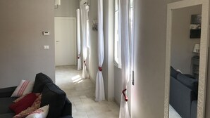 Un corridoio con un divano, tende bianche e una porta in fondo.