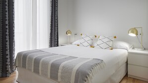 A neatly made bed with a striped blanket, two bedside lamps, and a white nightstand. - Always Easy I Kursaal (San Sebastián/Donostia)