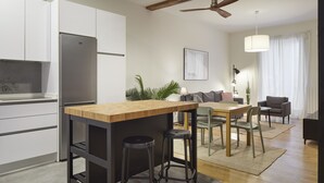 A modern kitchen with a wooden island, bar stools, a dining area with a table and chairs, and a ceiling fan. - Always Easy I Kursaal (San Sebastián/Donostia)