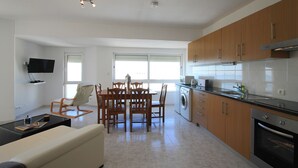 Eine moderne Küche mit Holzausstattung, einem Essbereich mit Tisch und Stühlen, einem an der Wand montierten Flachbildfernseher und einem eingebauten Backofen.