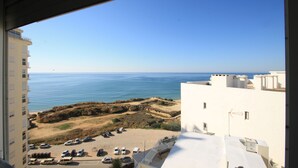 Blick aus einem Fenster auf eine Küstenlandschaft mit Gebäuden, parkenden Autos und dem Meer.