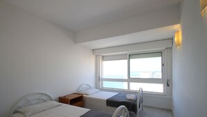Ein Schlafzimmer mit zwei Betten, einem Fenster mit Meerblick und einem kleinen Tisch mit Stuhl.