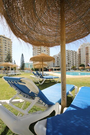 A poolside area with lounge chairs and umbrellas, surrounded by tall buildings.