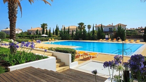 Une piscine avec des chaises longues, des palmiers et un ciel dégagé.