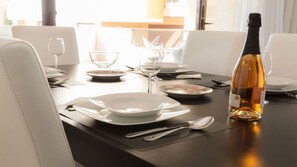 Een eettafel gedekt voor twee personen, met borden, glazen en een fles wijn.