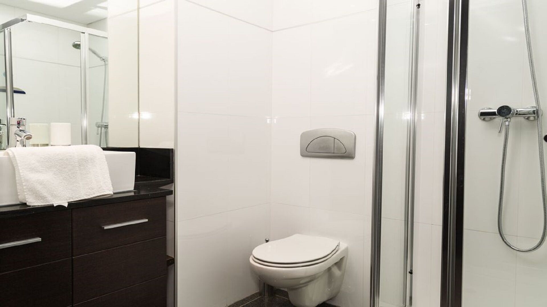 A modern bathroom with a glass shower enclosure, a toilet, and a vanity with a towel.
