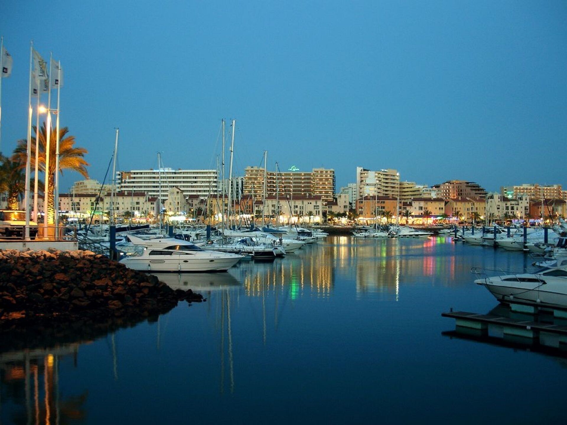 A marina with boats docked, surrounded by buildings and palm trees.