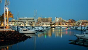 Un port de plaisance où sont amarrés des bateaux, entouré de bâtiments et de palmiers.