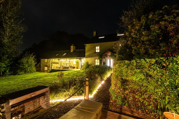 A house with a well-lit patio area, a barbecue grill, and a pathway leading to the entrance.