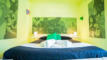 A hotel room with a bed, green walls, and superhero-themed artwork.