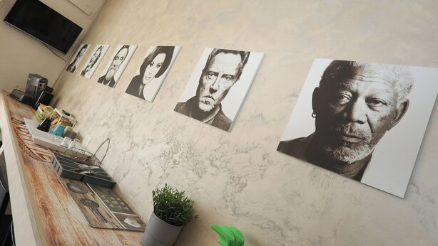 Eine Wand mit mehreren gerahmten Porträts, einem an der Wand befestigten Fernseher und einem Blumentopf auf einem Tisch.
