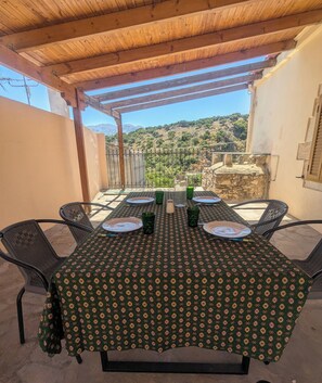 Un área de comedor al aire libre con una mesa para dos, rodeada de sillas, bajo una pérgola de madera.