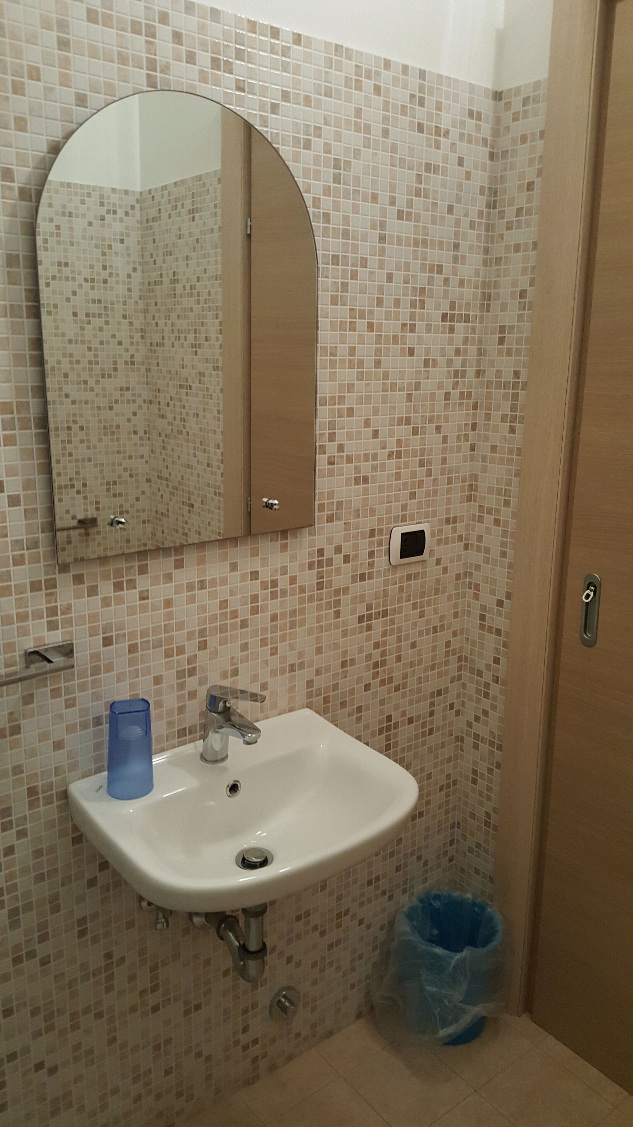 Un baño con lavamanos blanco, un espejo encima y pared de azulejos.