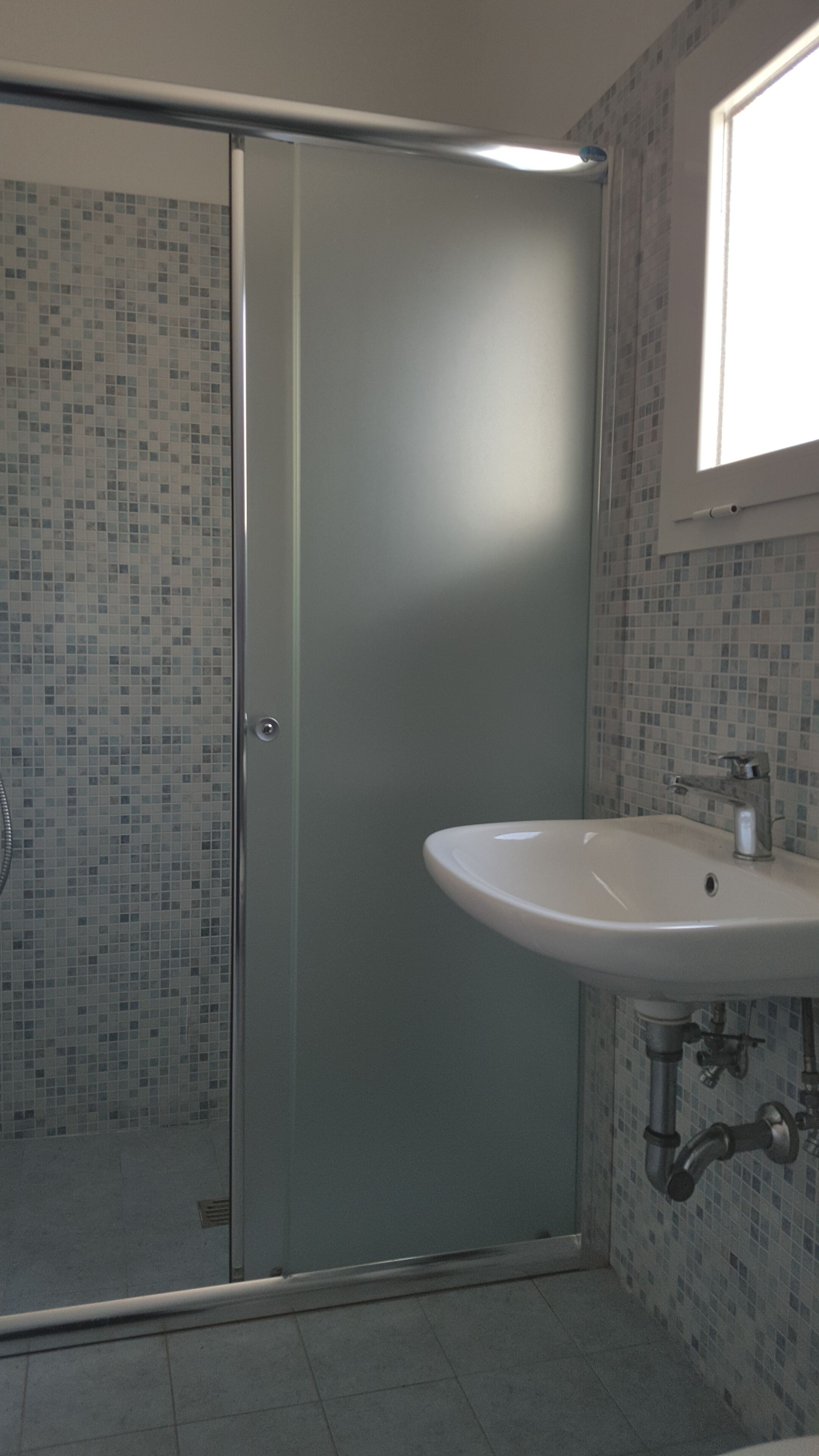 A bathroom with a glass shower door, a sink with a mirror above it, and tiled walls.