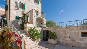 Un bâtiment en pierre doté d’un balcon, d’un escalier et d’un petit jardin.