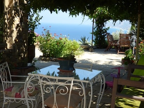 An outdoor patio with a table and chairs, surrounded by potted plants and a view of the sea.