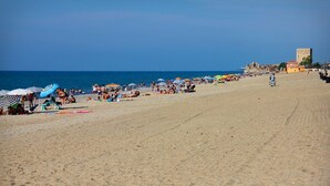 Une vaste plage de sable, parsemée de parasols et fréquentée par de nombreuses personnes.