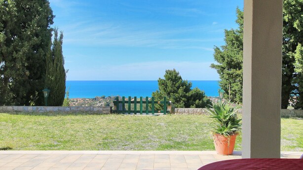 Une terrasse avec vue sur la mer, un mur en pierre et une clôture en bois peinte en vert.