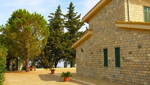 Un bâtiment en pierre avec une allée gravillonnée, des plantes en pot et des arbres.