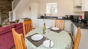 A cozy dining area with a round table set for two, a kitchen with white cabinets and a stone wall, and a staircase leading to an upper level. - Bowes Barn 4 Star near Beamish, Newcastle & Durham - Sleeps 3 -  Dogs Welcome  (Gateshead)