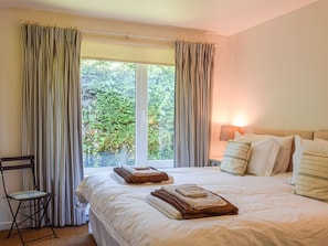 Quarto com cama grande, duas almofadas, uma cadeira e janela com cortinas.