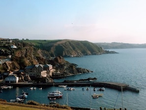 Uma vila costeira com casas numa encosta, um porto com barcos e um mar calmo.