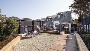 A backyard with a patio area, two lounge chairs, a small table, and a wooden fence. - Flip Flops - Three Bedroom Cottage, Sleeps 6 (Crantock)