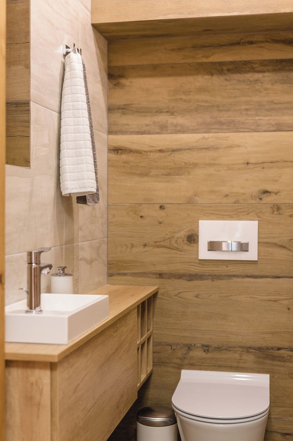 Une salle de bain moderne avec un meuble-lavabo en bois, un lavabo blanc, une serviette et des toilettes.